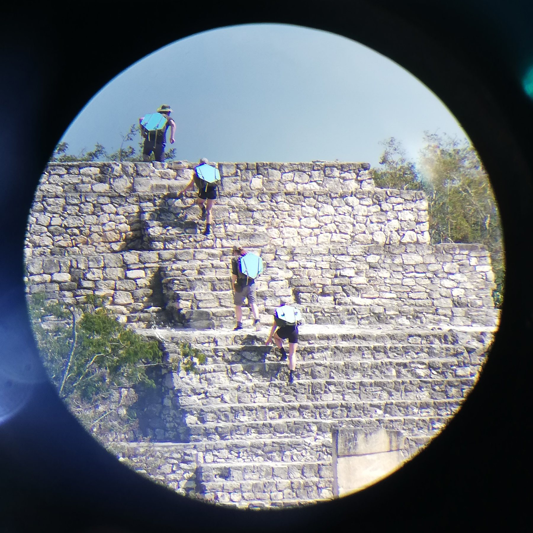 Figures on the Maya ruins at Calakmul, framed through an optical sight